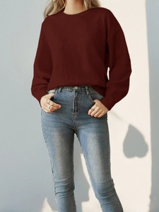Detail of burgundy knitted crewneck sweater and slim blue jeans outfit on model