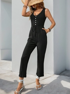 Detail of black textured sleeveless jumpsuit featuring front buttons and drawstring waist
