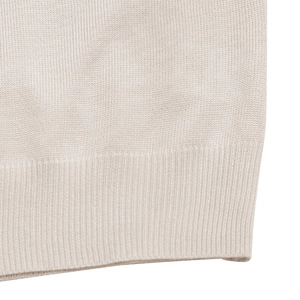 Detailed macro view of the cream-white knitted fabric and rib-knit hem of the sweater