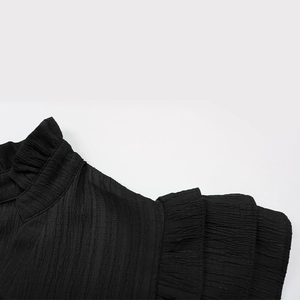 Close-up of textured black dress featuring ruffled stand collar and layered sleeve details