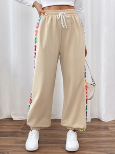Detail of beige joggers with colorful crochet floral embroidery stripes and drawstring waist