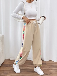 Detail of khaki sweatpants featuring colorful crochet side stripes and drawstring waist