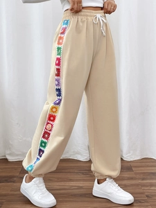 Detail view of beige joggers with colorful crochet pattern side stripes and waist drawstring