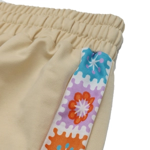 Detail of elastic waist and colorful floral side tape on beige casual knit trousers
