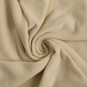 Close-up of beige knit fabric texture showing flexible spiral folds and smooth drape