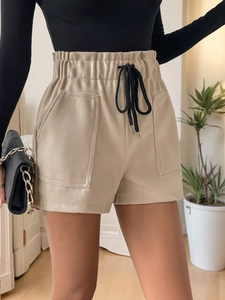 Detail view of beige high-waisted shorts with elastic waist and black drawstring
