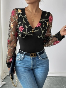 Detail of sheer mesh long sleeves with colorful floral embroidery on a black bodysuit