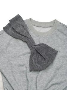 Detail of grey sweatshirt showing the ribbed round neck and a large glittery dark grey bow