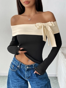 Detail of off-shoulder neckline with a large cream bow on a black long sleeve top