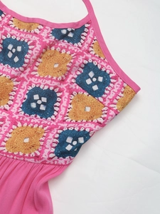Detail of pink halter dress showing colorful crochet pattern and pleated fabric texture
