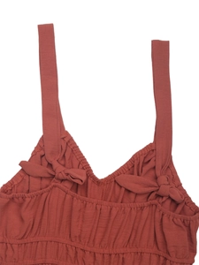 Detail of brick red pleated jumpsuit with bow decoration and V-neckline texture