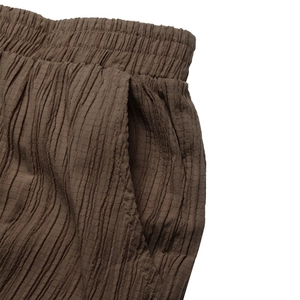 Dettaglio dei pantaloni marroni in tessuto stropicciato con vita elastica e tasche laterali