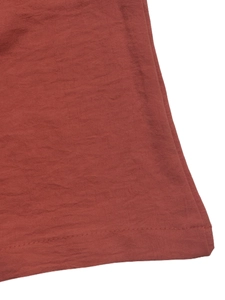 Macro shot of rust red pleated fabric jumpsuit showing detailed hem and double stitching