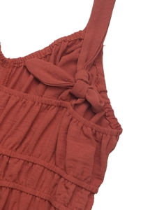 Macro detail of rust-red ruched fabric texture with decorative bow on a jumpsuit