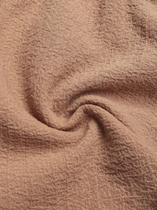 Detailed macro view of textured seersucker fabric in terracotta brown with ruffle layers