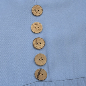 Close-up of five natural wood buttons on the light blue twill fabric of the dress