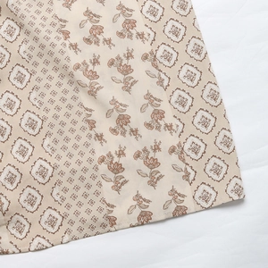 Close-up of lightweight fabric showing vintage floral and geometric patterns on a beige base