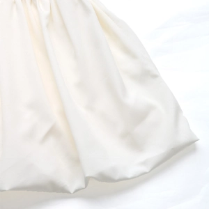 Detailed close-up of white textured dress fabric with elegant waist pleat design