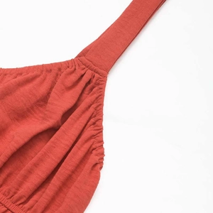 Close-up of rust red pleated dress showing fabric texture and stitched wide shoulder strap
