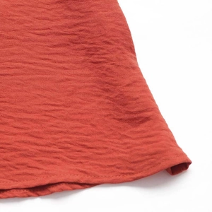 Detail of rust red textured fabric with pleated design and fine hem stitching on dress