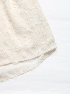Detail of cream ruffle dress featuring textured feather jacquard and soft fringe hem