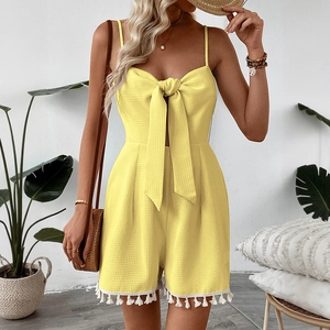Detail of yellow waffle knit romper featuring white tassel trim and front bow tie design