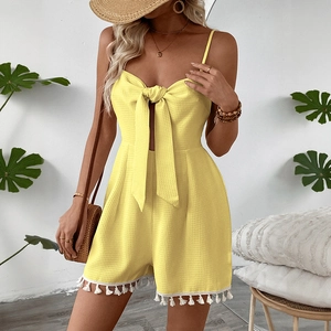 Detail of yellow waffle knit romper featuring a front tie bow and white tassel trim