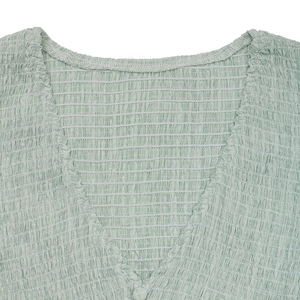 Detail of light green V-neck dress featuring smocking fabric texture and covered button