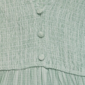Detail of light green smocked V-neck dress featuring fabric buttons and textured fabric