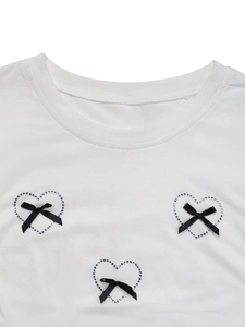 Close-up of white T-shirt featuring rhinestone heart patterns and black silk bows