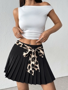 Detail of white off-shoulder top and black pleated skirt with leopard print bow belt