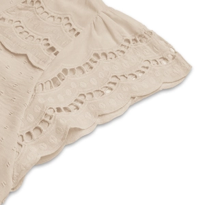 Detailed macro view of beige fabric with texture dots and embroidered eyelet lace edge