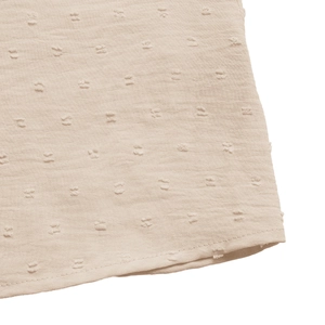 Macro detail of beige Swiss dot fabric texture and stitched hem on the summer shirt