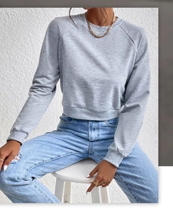 Detail view of a grey cropped crewneck sweatshirt paired with light blue distressed denim