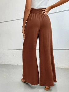 Detail of high waisted smocked waistband on brown wide leg trousers for women