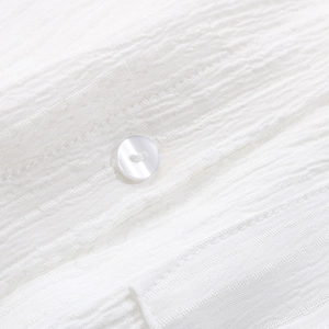 Close-up of white pearlescent button and seersucker textured fabric on a long sleeve shirt