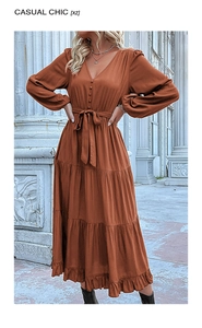 Detail of rust red long sleeve tiered dress featuring V-neckline and belted waist