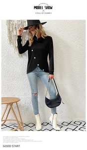 Detail of black knit top with turtleneck design and decorative white buttons on the hem