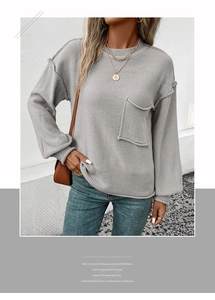 Detail of grey crewneck knit sweater featuring exposed shoulder seams and front pocket