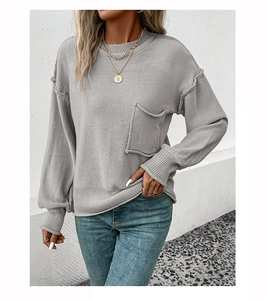 Detail view of grey knit sweater with raw-edge chest pocket and ribbed crew neck finish