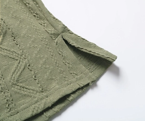 Détail du haut en tricot vert montrant le tissu jacquard texturé et l'ourlet à fente latérale