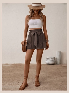 Detail view of high-waisted brown linen shorts featuring a tie-knot bow and ruffled edges