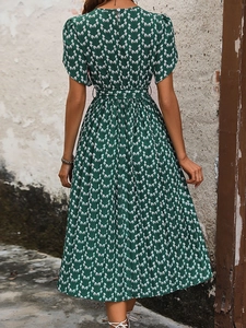 Robe plissée évasée à fleurs vert foncé avec ceinture, vue de dos sur fond mural en pierre