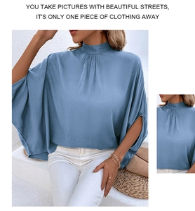 Detail of blue satin mock neck blouse featuring elegant pleats and batwing sleeve design