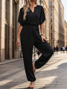 Outdoor street view of a black short sleeve V-neck jumpsuit with elastic waist and cuffs