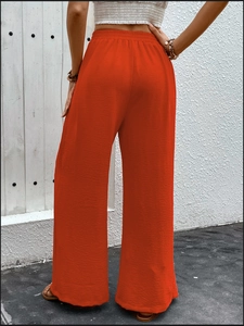Detail of high waisted wide leg pants in orange-red featuring textured fabric and elastic waist