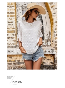 Detail of white chiffon top featuring 3D flocked polka dots and ruffle sleeves against stone wall