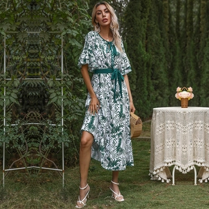 Floral V-neck maxi dress with tropical leaf print and green waist belt in garden setting