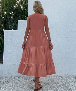 Back view of a sleeveless coral tiered maxi dress in a resort-style garden setting