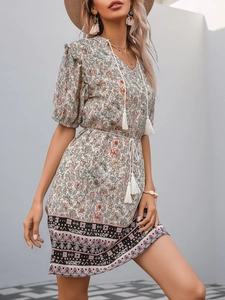 Detail of V-neckline with white tassels and floral pattern on bohemian summer dress